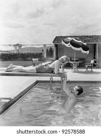 Young Woman Lying On A Diving Board With A Young Man Hanging From It