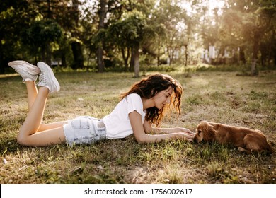 Young woman lying on green grass with her little dog, cocker spaniel breed puppy, outdoors, in a park.