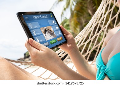 Young Woman Lying On Hammock Using Smart Home Automation On Digital Tablet At Beach