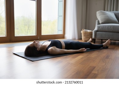 Young woman lying on mat listens meditative music through earbuds practicing asanas at home, do Corpse Savasana Dead Body, relaxing after yoga training. Repose, boost inner balance, no stress concept - Shutterstock ID 2132760011