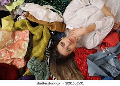 Young Woman Lying On Pile Of Different Clothes, Top View. Fast Fashion Concept