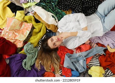 Young Woman Lying On Pile Of Different Clothes, Top View. Fast Fashion Concept