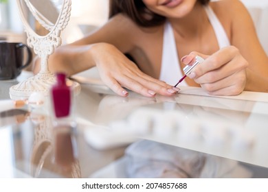 Young woman lying on sofa and doing her nails. Woman applying nail polish at home in sunny day. Domestic spa procedures concept. Enthusiastic Female Painting Her nails - Powered by Shutterstock