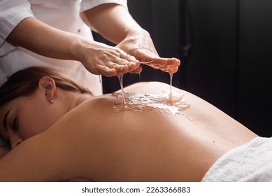 young woman lying on the table and getting spa procedure massage with honeyed in dark room. Masseuse pours honey on client's back. relaxing and beneficial spa treatments for the skin - Powered by Shutterstock