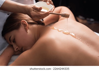 young woman lying on the table and getting spa procedure massage with honeyed in dark room. Masseuse pours honey on client's back. relaxing and beneficial spa treatments for the skin - Powered by Shutterstock