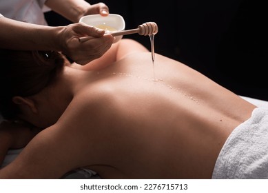 young woman lying on the table and getting spa procedure massage with honeyed in dark room. Masseuse pours honey on client's back. relaxing and beneficial spa treatments for the skin - Powered by Shutterstock