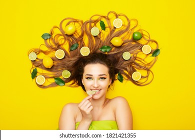 young woman lying on yellow background with citrus fruits on long hair, bites lemon wedge, food taste, energy - Powered by Shutterstock