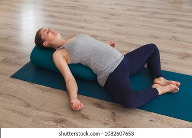 Young Woman Lying On Yoga Mat Using Bolster Cushion