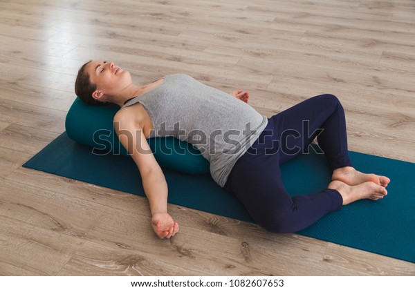Young woman\
lying on yoga mat using bolster\
cushion