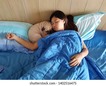 Young woman is lying and sleeping with pug dog in bed