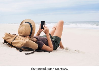 Young woman lying with smart phone on a beach. Girl looking at mobile phone. Relaxation, connection, social distance, mobile apps, rest, vacations, holidays, online shopping concept - Powered by Shutterstock