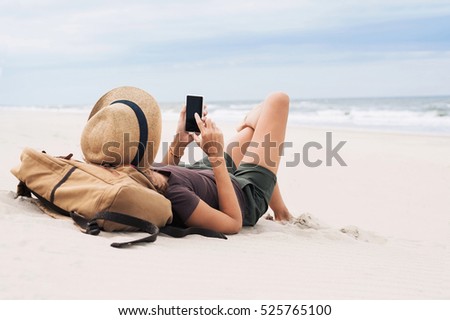 Young woman lying with smart phone on a beach. Girl looking at mobile phone. Relaxation, connection, social distance, mobile apps, rest, vacations, holidays, online shopping concept