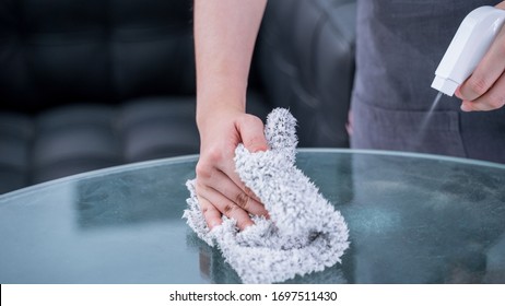 Young Woman Maid In Apron Is Cleaning, Wiping Down Office Glass Table Surface With Spray Bottle Cleaner, Wet Rag, Close Up, Lifestyle, Real People.