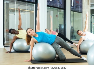 Young Woman Maintaining Active Lifestyle Exercising With Gym Ball During Group Pilates Class In Modern Fitness Center