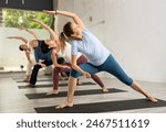 Young woman maintaining mental and physical health attending group yoga class at studio, practicing stretching poses
