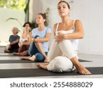 Young woman maintaining mental and physical health attending group yoga class at modern studio, practicing twisting poses