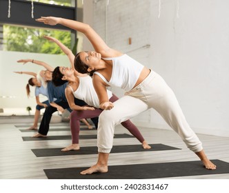 Young woman maintaining mental and physical health attending group yoga class at modern studio, practicing twisting poses - Powered by Shutterstock