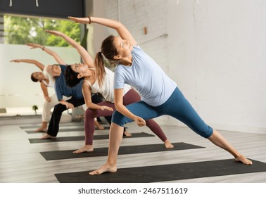 Young woman maintaining mental and physical health attending group yoga class at studio, practicing stretching poses - Powered by Shutterstock