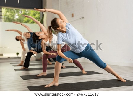 Young woman maintaining mental and physical health attending group yoga class at studio, practicing stretching poses