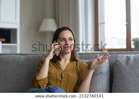 Young woman make call sit on sofa at home. Attractive female holding smartphone, having pleasant conversation to friend, share news and plans enjoy distancing communication. Connection, tech concept