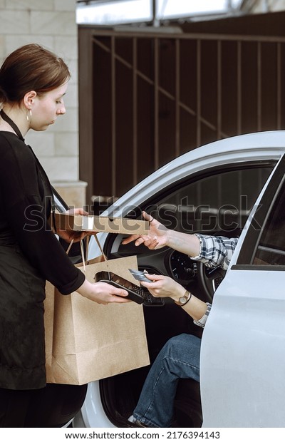 a young woman makes a\
purchase of ready-made food on a pre-order in her car, the courier\
drives her to the car, pays for the purchase online through the\
terminal