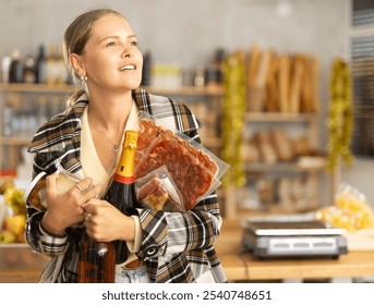 Young woman makes purchases in the supermarket. Smiling woman with alcohol, cheese and meat in a deli. Customer buys delicious food and snacks - Powered by Shutterstock