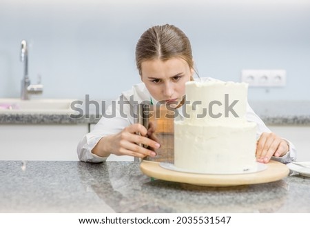 Young woman makes a wedding cake with white cream  using a  cooking spatula.