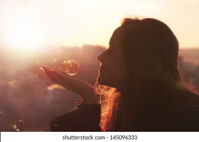 Young woman makes a wish. Cityscape background at sunset.