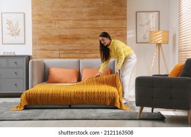 Young Woman Making Bed In Room. Modern Interior With Sleeper Sofa