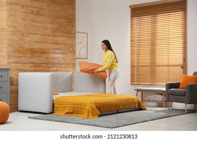 Young Woman Making Bed In Room. Modern Interior With Sleeper Sofa