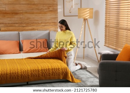 Young woman making bed in room. Modern interior with sleeper sofa