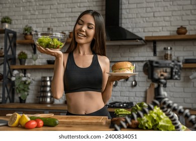 Young woman making choice to eat healthy food in kitchen for her vlog, comparing junk fatty unhealthy meal with raw eating, vegetable salad online on stream live - Powered by Shutterstock