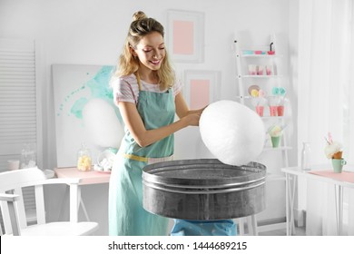 Young woman making cotton candy using modern machine in room