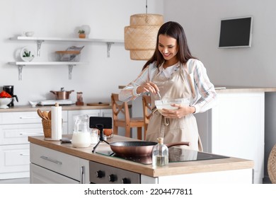 Young Woman Making Dough For Pancakes While Following Video Tutorial In Kitchen