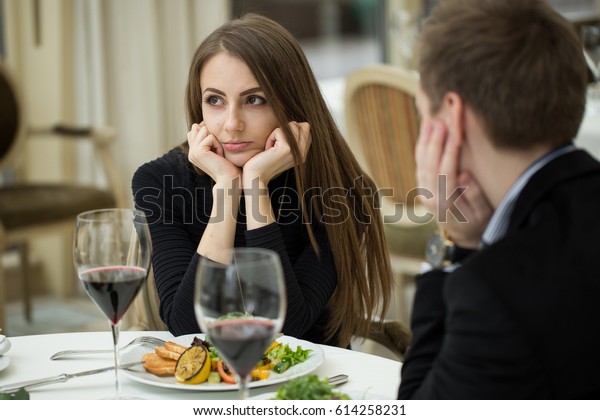 Young woman making an exasperated expression\
gesture on a bad date at the\
restaurant