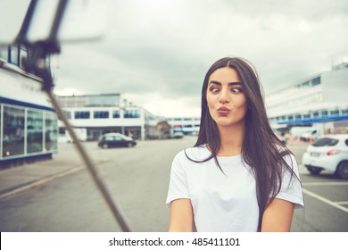 Young Woman Making A Goofy Cross Eyed Puckered Lips Self-portrait Outdoors Using A Smartphone At The End Of A Selfie Pole Stick