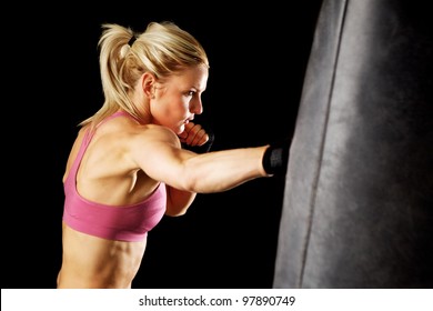 Young Woman Making A Hard Punch On A Punching Bag. Isolated On Black.