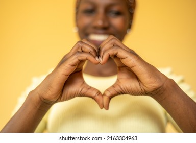 Young woman making a heart shaped symbol while smilling with a yellow background - Shutterstock ID 2163304963