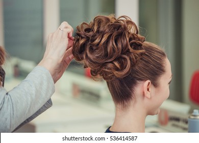 young woman making high bun hairstyle at hairdresser indoor shot