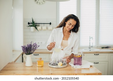 Young woman making lemonade in a kitchen of cozy house. Homemade healthy drink. Summer beverage.