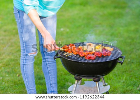 Young woman is making meat barbecue in the garden on the green grass - cooking healthy organic and non gmo food and family concept - chicken, beef, lamb and pork real BBQ with smoke