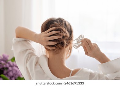 Young woman making messy hair bun, clipping hair with claw clip, back view, soft natural light, fashion hairstyle, girls daily beauty routine, lifestyle. - Powered by Shutterstock