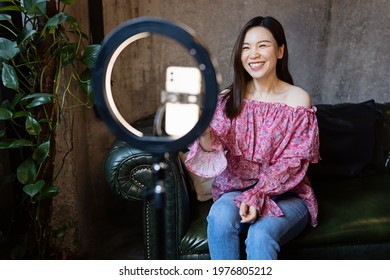 Young Woman Making Photo Or Video Content For Social Media With Smartphone And Light Of Ring Lamp. Beauty Blogger Smiles To Mobile Phone Screen. Influencer Makes Broadcast Communicates With Followers