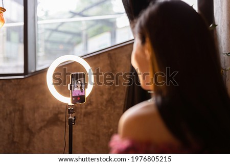 Young woman making photo or video content for social media with smartphone and light of ring lamp. Beauty blogger smiles to mobile phone screen. Influencer Makes broadcast communicates with followers