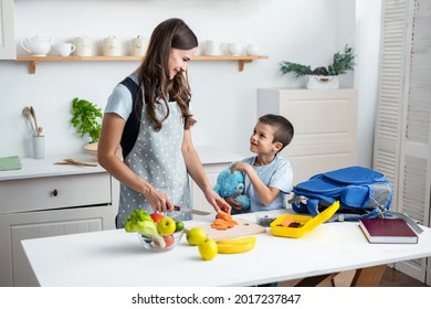 Young Woman Making School Lunch In The Morning. Mother With Son Preparing School Snack Or Lunch In Home Kitchen