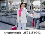 Young woman making selfie portrait standing with luggage at the modern railway or bus station. Concept of a transportation and urban life.