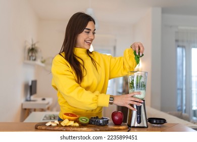 Young woman making smoothie with fruits. Beutiful girl standing in the kitchen and preparing smoothie with fruit and vegetables - Powered by Shutterstock