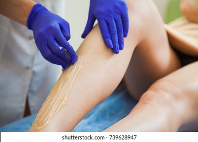 Young woman making sugaring hair removal procedure at beauty salon. Beautician cosmetologist make epilation with liquid sugar paste.