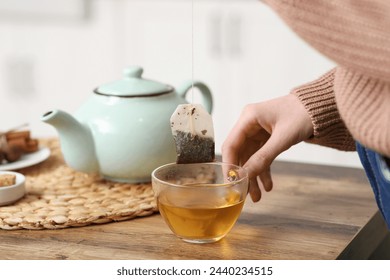 Young woman making tea with tea bag on table in kitchen