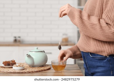 Young woman making tea with tea bag on table in kitchen